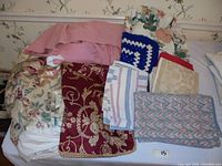 Photo showing 3 bed skirts including pink and floral patterns, along with 14 assorted pillowcases and shams in various fabrics and patterns.