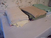 Eight folded blankets displayed on a table, showing variety in textures and colors with some crocheted blankets clearly visible.
