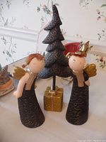 Photo showing two ceramic angel figurines with gold wings, and a ceramic Christmas tree with a gold gift wrapped base, all with black and gold swirl details.