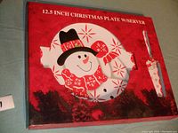 Red and white boxed 12.5 inch Christmas snowman cake plate with server showing snowman face and matching spreader decorated with snowflakes and holly berries.