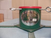 Green metal Christmas tree stand with red rim, close-up showing detailed label on stand.