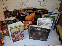 Cookbooks displayed upright and stacked, showing titles in English and German, depicting the lot's diversity in culinary themes and languages