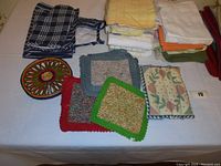General overview of folded and stacked kitchen linens including towels, placemats, and table runners, plus crocheted trivets laid flat