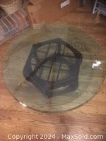 Top view of thick beveled edge round glass tabletop with hexagonal wooden base visible beneath.