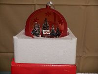Large red spherical Mr. Christmas musical lighted ornament in its original white foam packaging and red box, with winter scene inside including trees and Santa figure.