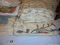 Multiple folded fabric window treatments stacked, showing floral prints and solid colors.