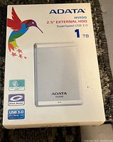 Original retail box of ADATA HV100 1TB external hard drive showing front with product image and specifications.