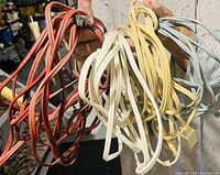 Photo showing four assorted flat extension cords in red, white, yellow, and light blue colors being held by a person.
