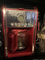 Photo of Bella coffee maker showing red housing, glass carafe, and front stainless steel control panel with buttons.