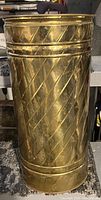Tall cylindrical brass bucket with etched diagonal and horizontal decorative lines forming a lattice pattern.