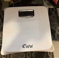 White digital bathroom scale with an electronic display and 'WW' logo on a carpeted floor.
