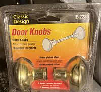 Photo of retail packaged classic design door knobs set E-2280 made of brass plated steel, showing front package with product info.