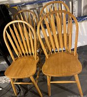 Four solid wood dining chairs arranged together showing the curved spindle backs and contoured seats.