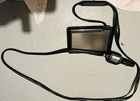 Photo of black Garmin GPS device connected to a car charger power cord with cigarette lighter adapter.