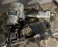 Photo of Hitachi brad nailer showing metal body, black plastic parts, attached hose fitting, and strip of brad nails loaded in the tool.