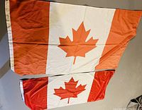 Two Canadian flags laid flat with one partially overlapping the other, showing their red maple leaf design and red and white vertical bands.