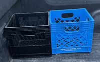 Photo of two plastic milk crates, one black and one blue, side by side in a truck bed.