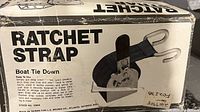 Ratchet strap in original box showing the product name, application for boat tie down, strap with hooks illustration, and manufacturer info.