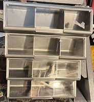Front view of gray plastic organizer box with clear sliding lids and multiple compartments for screws and nails.