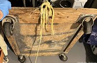 Bottom view of the wooden dolly showing the four metal swivel casters attached to the wooden platform and the rope tied through a hole in the wood.