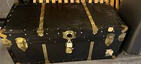 Closed view of the black steamer trunk showing brass hardware on corners and locks.