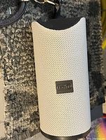 White Teufel Bluetooth speaker with black accents resting on carpet, showing carry strap attachment.