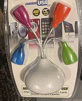 Photo of USB 2.0 4-port hub showing white base, four colored port covers (purple, orange, blue, green), flexible silver connectors.