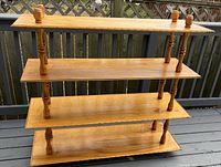 Photo of a wooden display shelf showing its front view with four wooden shelves and turned spindle supports on a deck background.