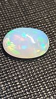 Close-up photo of a single oval cabochon Ethiopian opal showing vibrant multicolored fire on black textured background.