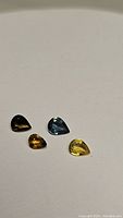 Four pear-shaped sapphires in varying shades of blue and yellow on a neutral background.