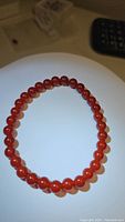 A single stretchy bracelet composed of spherical carnelian beads in a rich fire orange red color, displayed on a white surface.