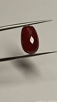 Close-up of the carnelian gemstone held in tweezers showing dark red-orange color and faceted surface.