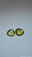 Pair of fancy cut yellow and green multicolored sapphire gemstones photographed on a neutral background with light reflections showing clarity and color.