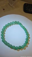 Clear top-down view of the green aventurine beaded bracelet with evenly sized round beads on a stretchy band, laid flat on a white surface under bright lighting.