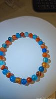 Full view of the round blue and red agate beads on a stretchy bracelet arranged in a circle on a white plate.