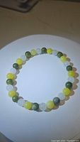 Photo of a multicolored natural jade bead stretchy bracelet laid out in a circle on a white surface, displaying the smooth round beads in white, yellow, and green colors.