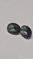 Pair of oval cut Mystic Topaz gemstones with purple rainbow coloration on a plain white background
