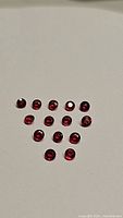 Group of 14 small round faceted rubies with vivid blood red color on a plain background.