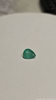 Single pear cut natural emerald gemstone shown on a white background, highlighting its size and color.