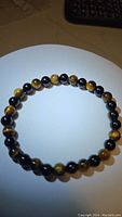 Photo of a circular stretchy bracelet made of alternating natural tigerseye and jet black onyx beads on a white background.