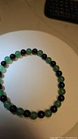 Natural gemstone bracelet with alternating black onyx and green aventurine beads placed on white surface, showing round polished beads and stretchy design.