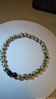 Top down image of bracelet laid flat showing circular shape and bead pattern of natural dalmatian jasper and 3 black onyx beads.