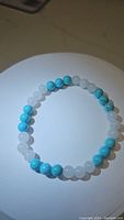Bracelet with alternating polished round white jade and blue turquoise beads arranged on a white circular display, lit from above.