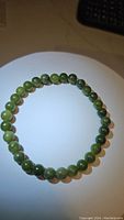Photo of a natural green jade bead bracelet arranged in a circle, showing polished round green beads with slight color variations.