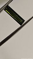 Close-up of the rectangular green tourmaline gemstone held by tweezers showing color and cut.