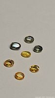 Photo showing seven natural oval cut sapphires in mint green and golden yellow shades arranged on a plain background.