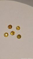 Five round-cut yellow sapphire gemstones on a white background, showing color and clarity.