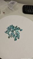 Multiple loose Paraiba blue apatite crystals on white surface showing their size, shape and color.