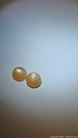Two round peach moonstone cabochon stones displayed on a plain surface, showing their size, shape, and flash effect under lighting.