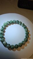 Top-view photo of the green spotted jasper bead bracelet arranged in a circular shape on a white surface with visible lighting shine.